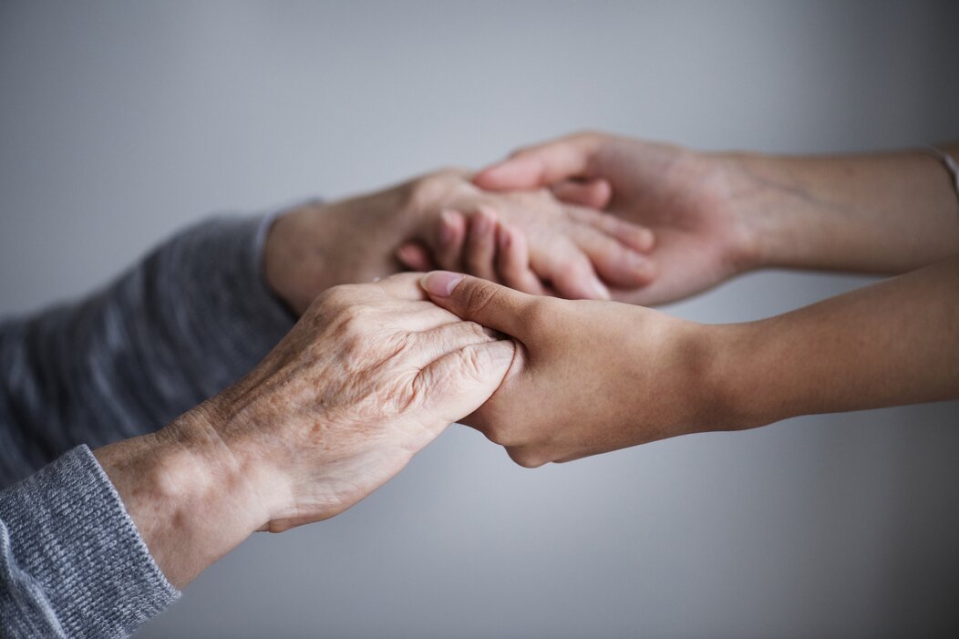 Photo d'une personne âgé et d'un personnel de santé se tenant les mains